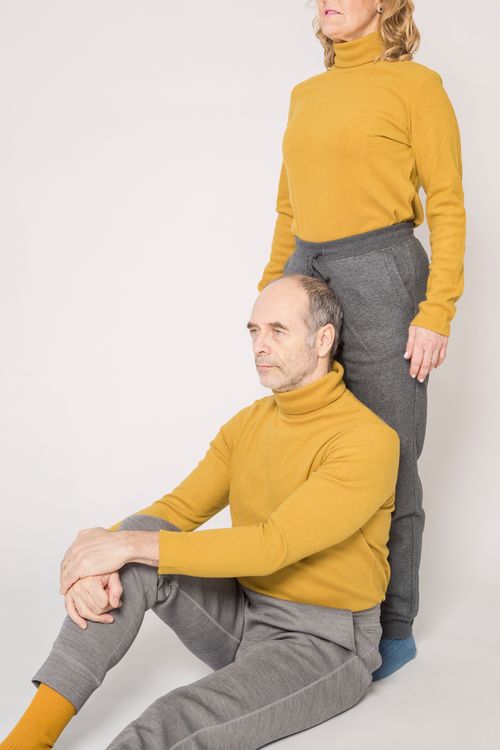 Free Senior couple posing in studio with yellow sweaters and gray pants for a relaxed photo session. Stock Photo