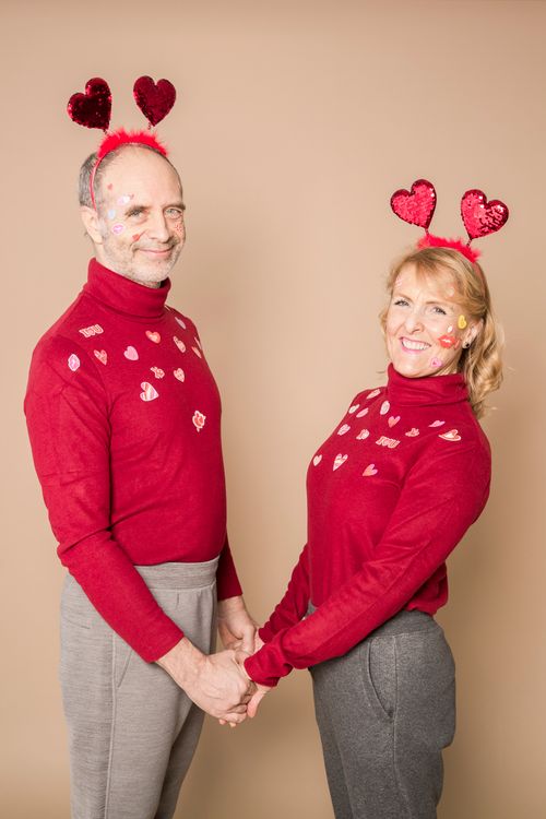Free Joyful senior couple in matching red outfits celebrating Valentine's Day with heart decorations and smiles. Stock Photo