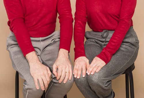 Free Crop unrecognizable mature man and woman in similar casual outfits sitting together on chairs with hands on knees against beige background Stock Photo