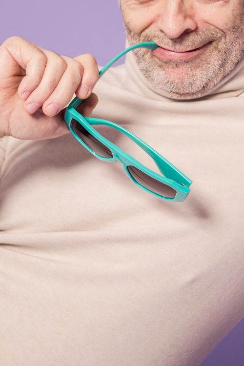 Free Charming elderly man playfully smiling while holding sunglasses against a purple studio background. Stock Photo