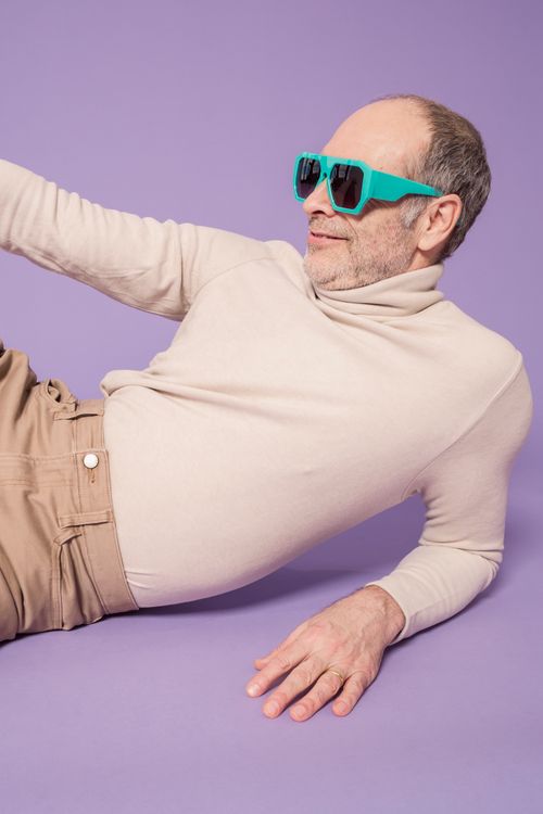 Free Elderly man in sunglasses and sweater smiling against a purple background. Stock Photo