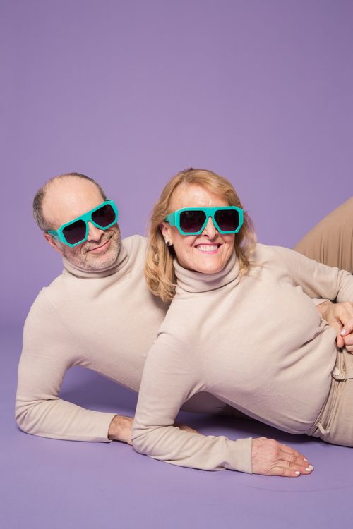 Free Elderly couple in matching sweaters and sunglasses, posing on purple background. Stock Photo
