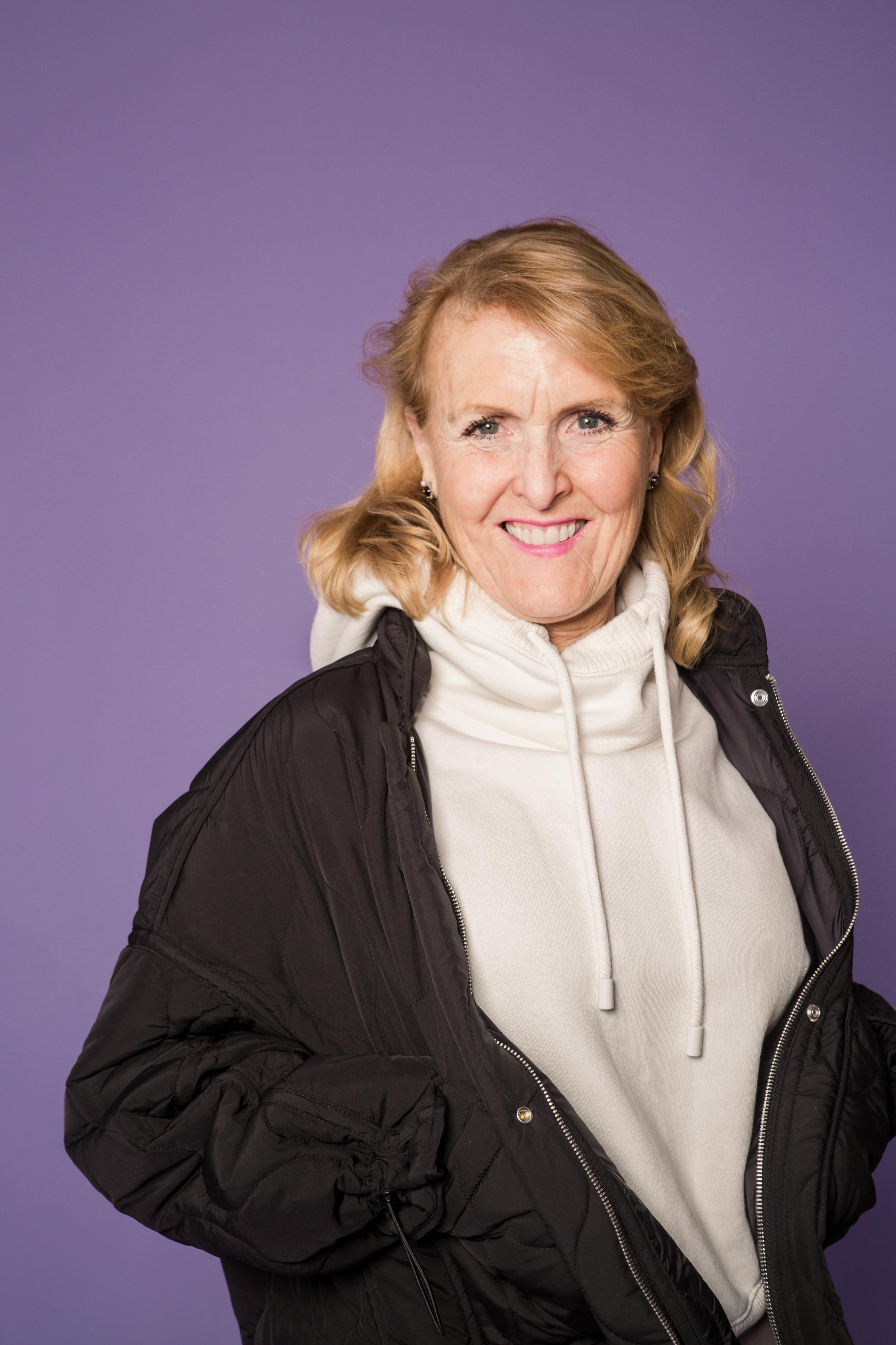Elderly woman smiling in studio wearing casual fashion against purple background.