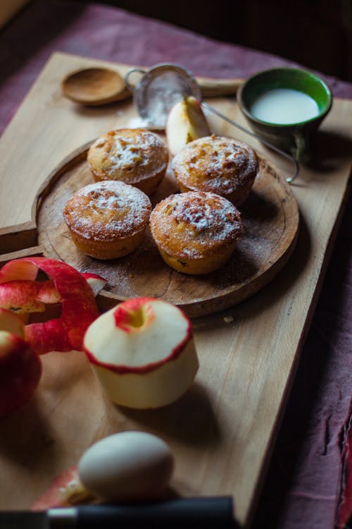 Free From above of delicious homemade cupcakes with powdered sugar placed near apples and cup with egg at kitchen Stock Photo