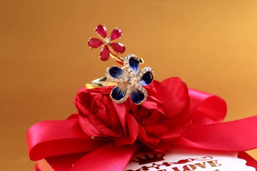 Close-up of floral design rings on a red ribbon gift box with vibrant flowers.