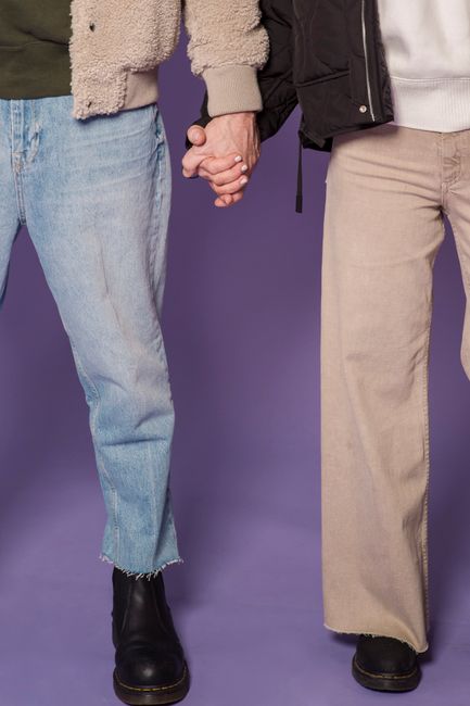 Two people holding hands in casual outfits against a purple studio backdrop.