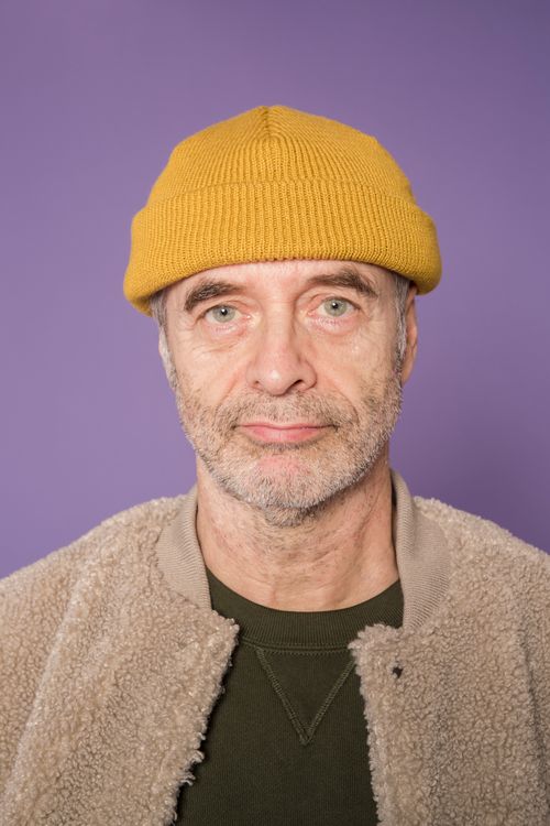 Free Close-up portrait of a senior man wearing a yellow beanie against a purple background. Stock Photo