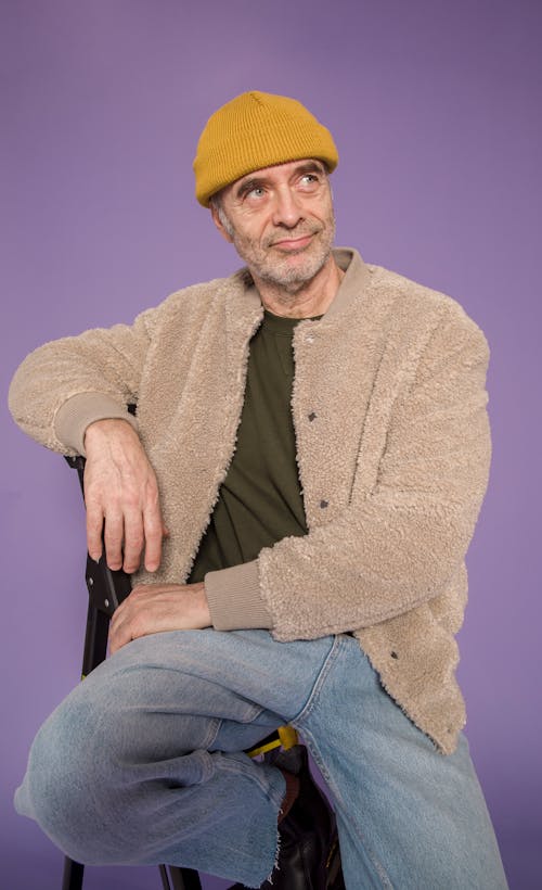 Man in Brown Coat and Blue Denim Jeans Sitting on Chair