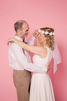 Joyful elderly couple embracing and dancing, set against a pink studio backdrop.