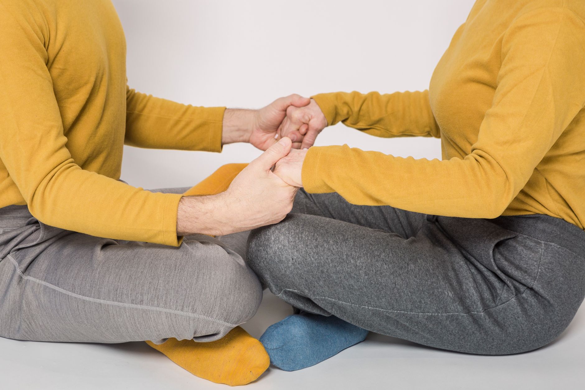 A couple in matching yellow sweaters holding hands while sitting cross-legged indoors.