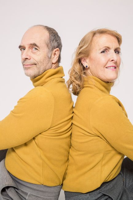 Senior couple sitting back-to-back, showcasing affection and togetherness indoors.