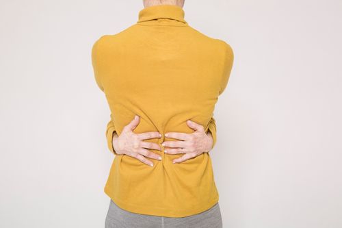 Free Man in a yellow sweater posing creatively by hugging himself in a studio setting. Stock Photo