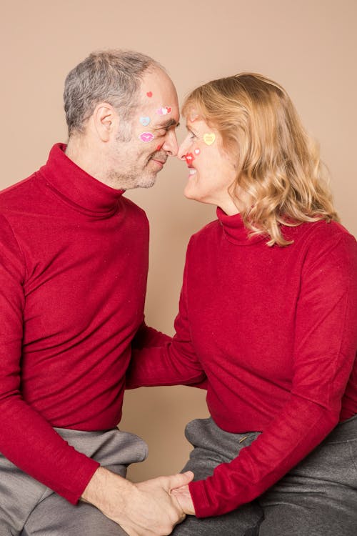 Happy senior spouses with painted faces smiling and holding hands in studio