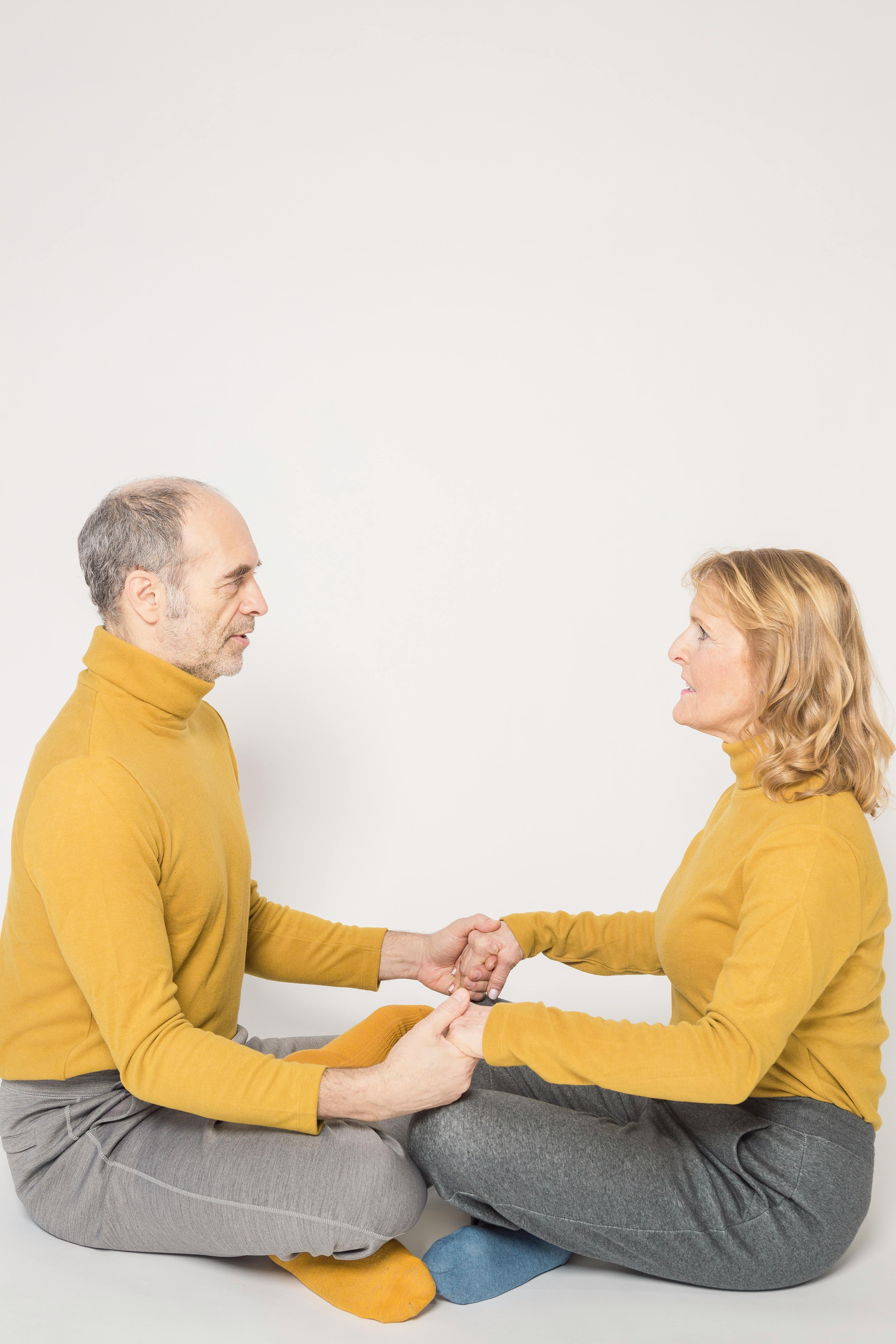 trendy elderly couple resting on floor with crossed legs and holding hands