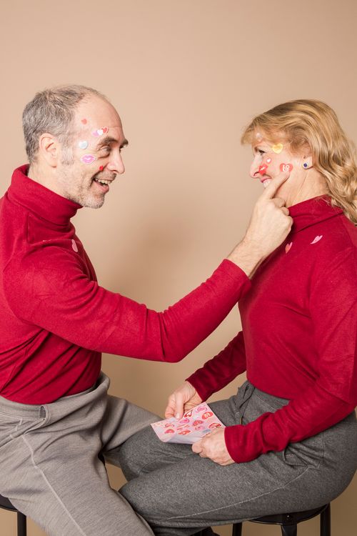 Free Senior couple in red sweaters sharing a playful moment with face stickers, indoors. Stock Photo