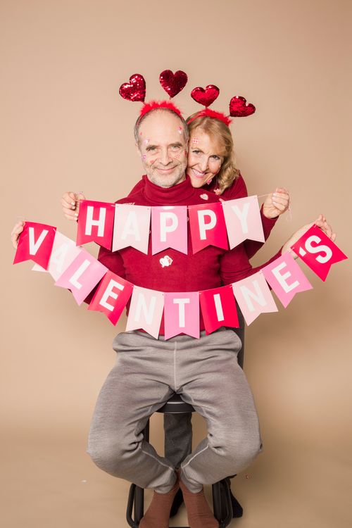 Free Elderly couple holding Valentine's banner, expressing love and joy in a studio setting. Stock Photo