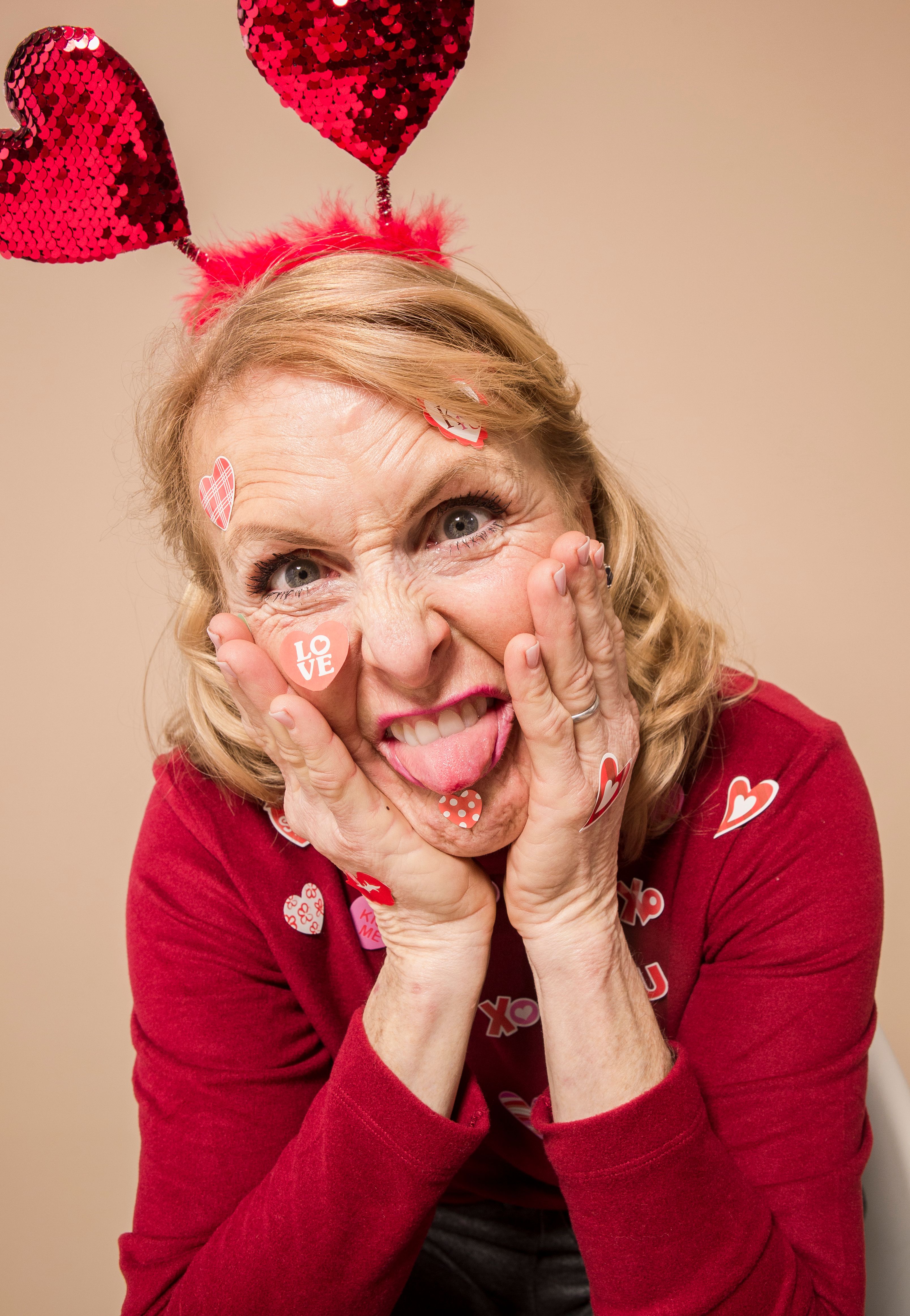 A humorous and playful portrait of a senior woman wearing Valentine's themed clothing and headband, making a funny face.
