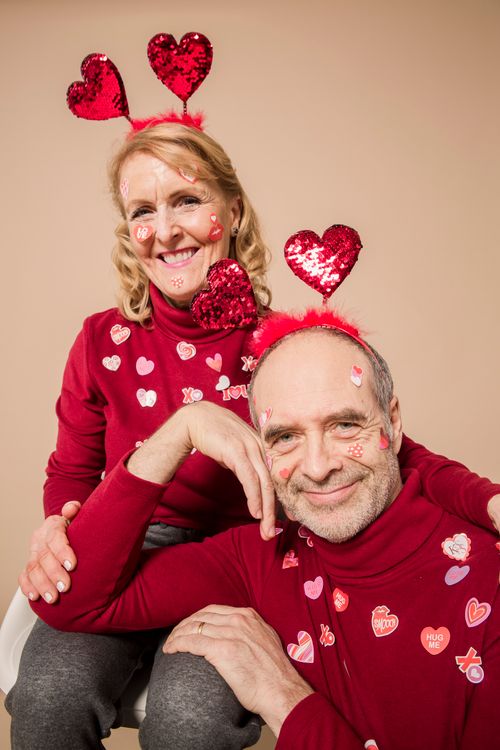 Free Elderly couple smiling in matching red Valentine outfits with heart accessories. Stock Photo