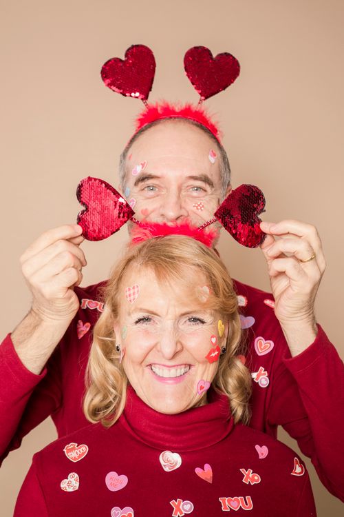 Free Senior couple in red with heart-themed headwear and sweaters celebrating Valentine's Day indoors. Stock Photo
