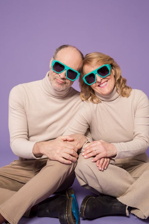 Free Joyful senior couple in matching beige outfits and turquoise sunglasses on purple background. Stock Photo