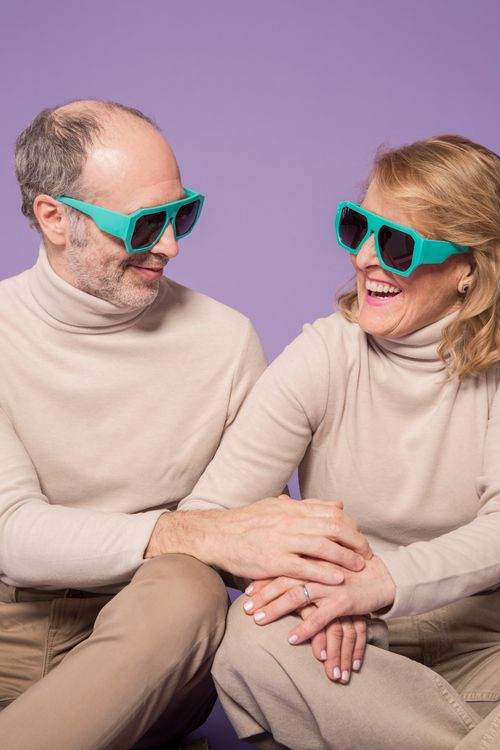 Free A cheerful elderly couple wearing matching sweaters and sunglasses. Studio setting with a purple background. Stock Photo
