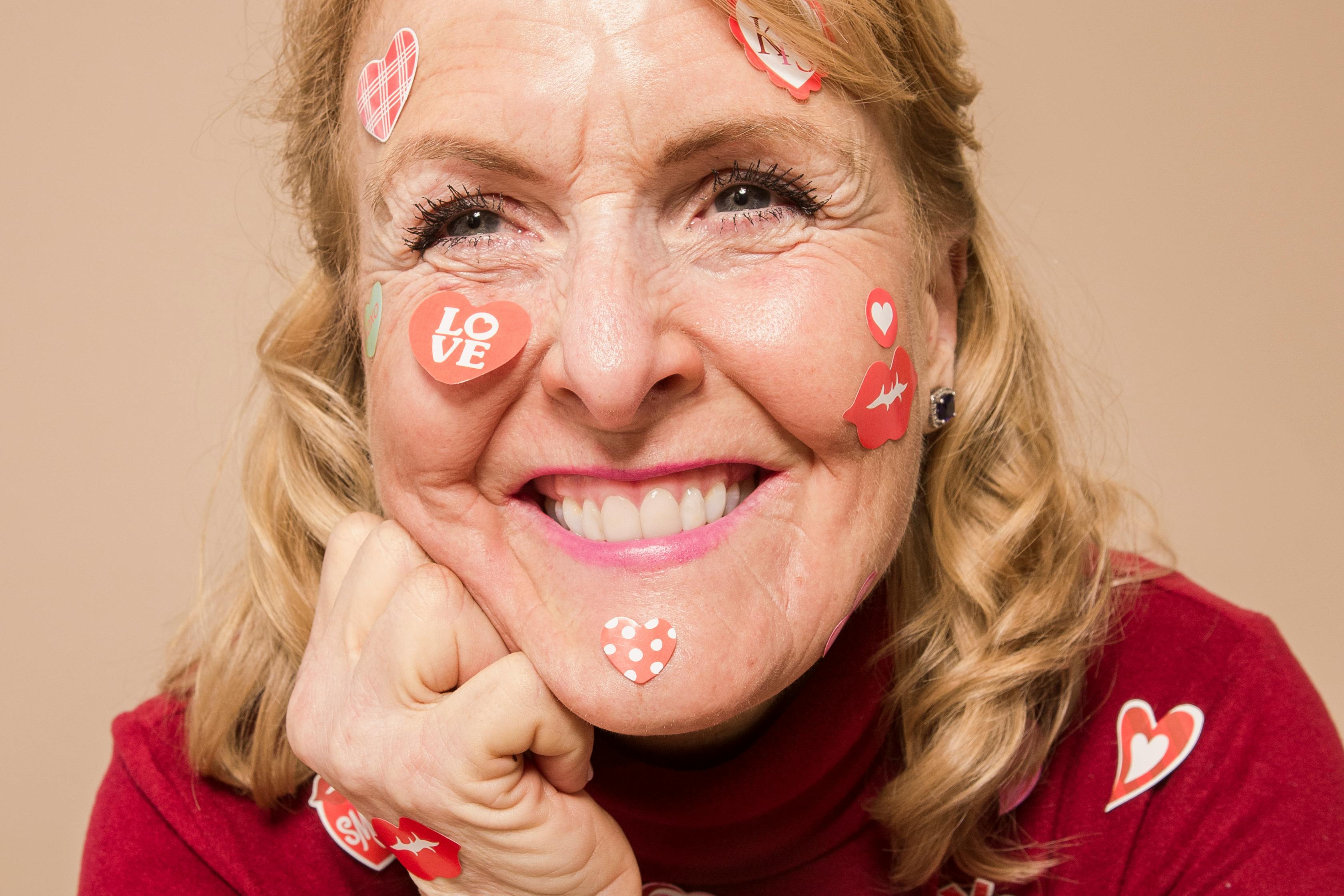 smiling senior lady with stickers on face in beige studio