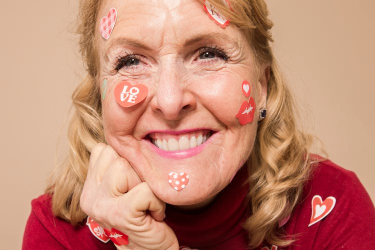 Smiling Senior Lady With Stickers On Face In Beige Studio