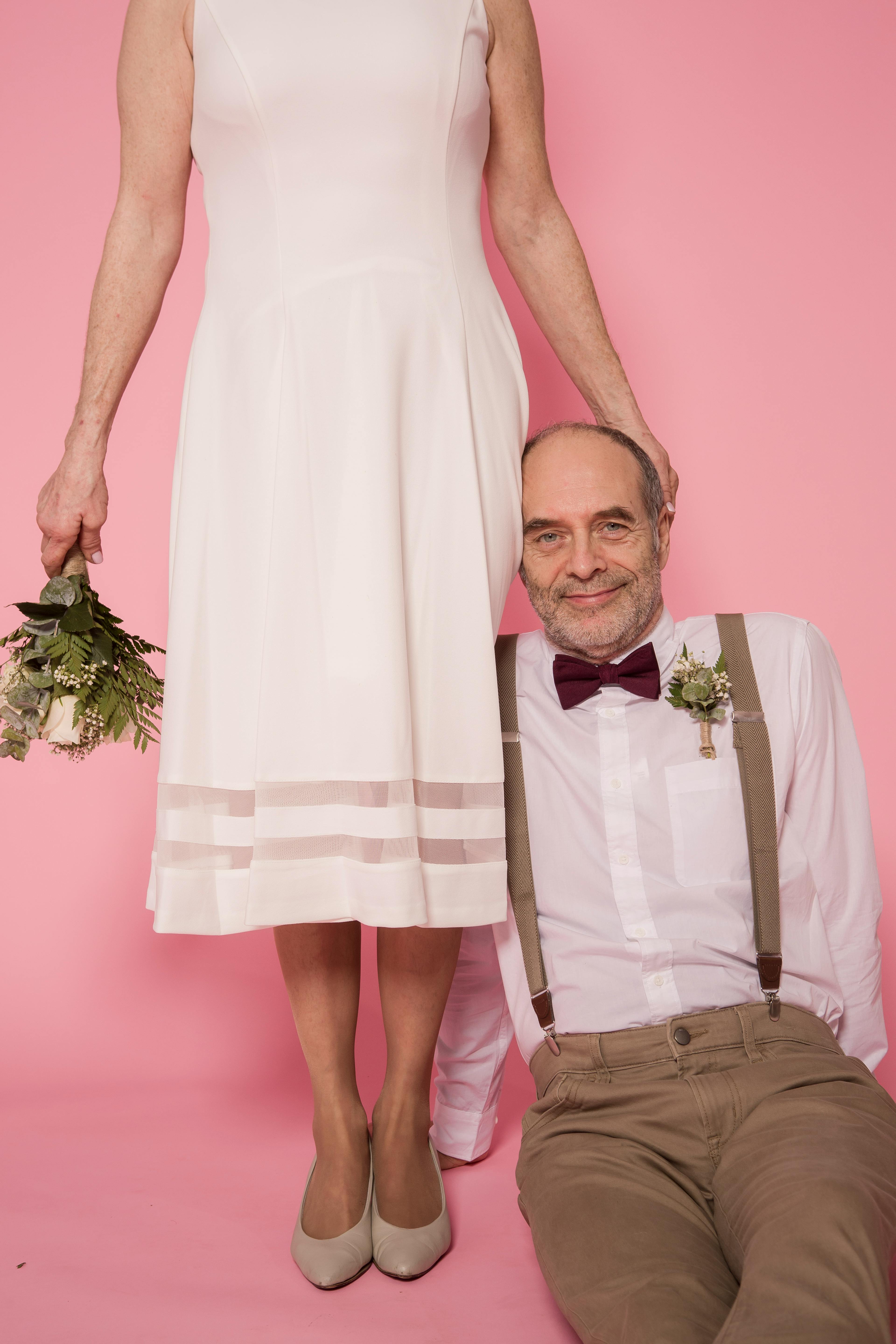 Elegant portrait of an elderly couple with wedding attire against pink background, showcasing love and joy.
