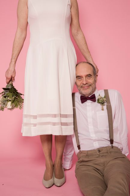 Elegant portrait of an elderly couple with wedding attire against pink background, showcasing love and joy.