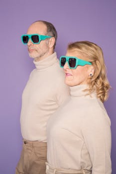 Senior couple wearing matching sunglasses and sweaters against a purple backdrop.