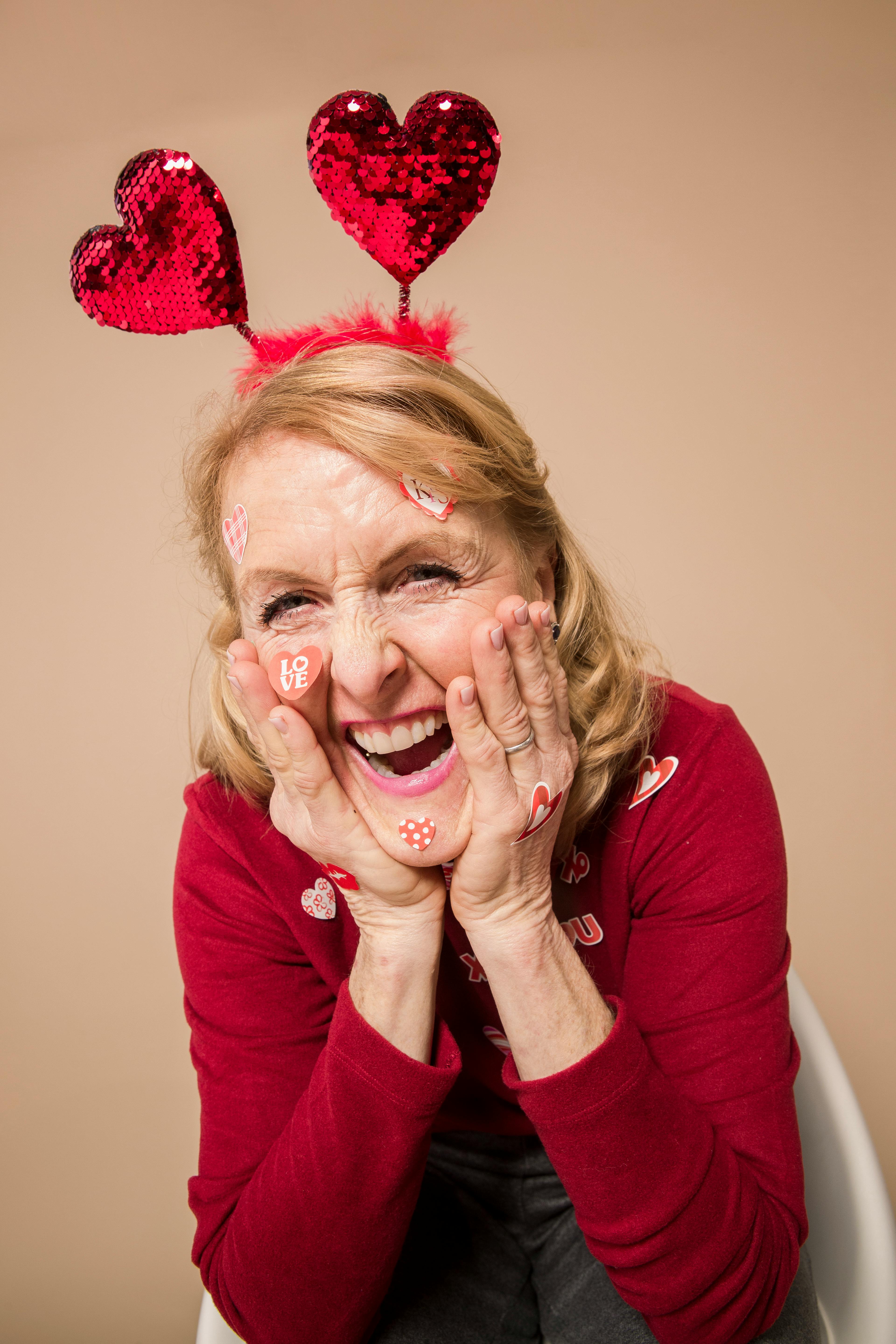 Elderly woman with heart headband and stickers celebrating Valentine's Day with joy and laughter.