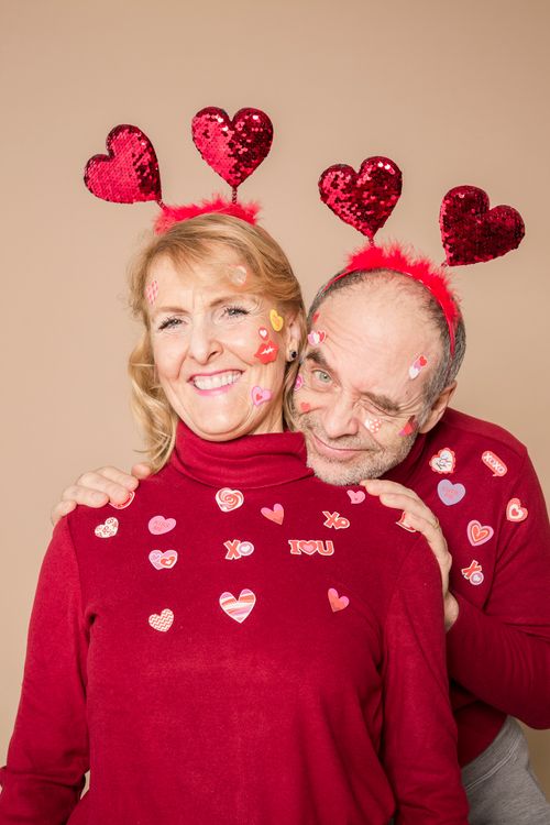 Free Senior couple in red sweaters with heart decorations enjoying Valentine's Day, smiling and embracing. Stock Photo