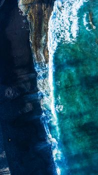 Stunning aerial shot of turquoise waves breaking on a rugged coastline, showcasing nature's beauty.