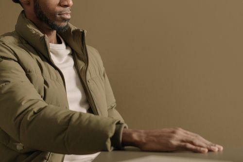 Free Portrait of a man in an olive jacket with hand calmly resting on the table. Stock Photo