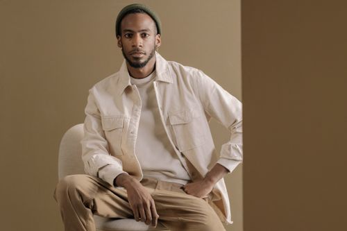 Free Portrait of a stylish man in modern attire and minimalist setting. Warm tones and neutral background enhance the sophisticated vibe. Stock Photo