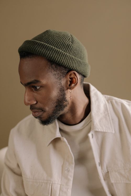 Free Side view of a bearded man wearing a green beanie and white jacket, indoor setting. Stock Photo