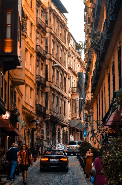 Travelers on narrow city street with aged buildings and cars riding on road in daytime