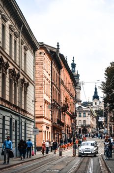 Travelers on sidewalk in city street with road with cars near historic buildings in daytime