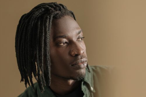Free Close-up portrait of a young man with braided hair looking away, showing thoughtful expression. Stock Photo