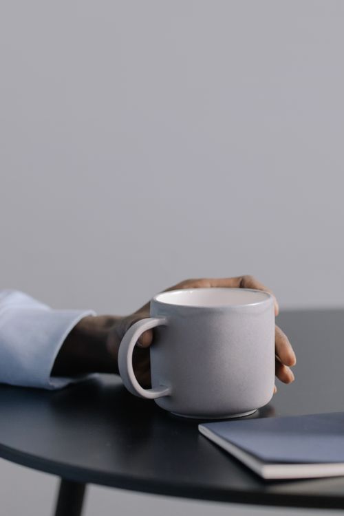 Free A hand holding a ceramic mug on a table, conveying a minimalist and relaxed atmosphere. Stock Photo