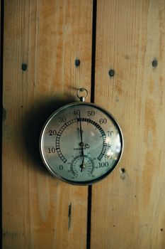 Vintage thermometer displaying temperature in Celsius and Fahrenheit mounted on wooden wall.