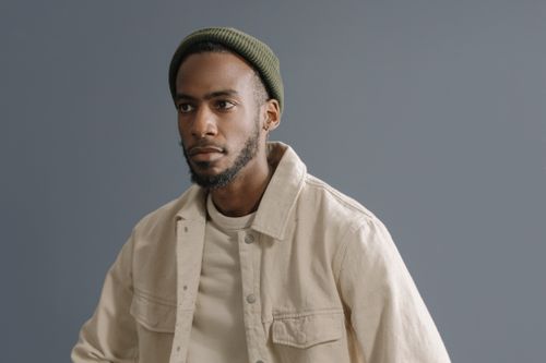Free Portrait of an African American man wearing a green beanie and beige jacket in a studio setting. Stock Photo