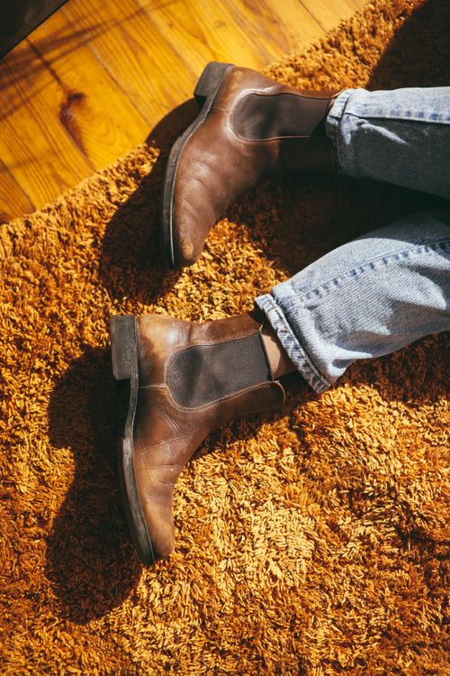 Free Close-up of vintage brown leather boots on a textured orange rug with wooden floor. Stock Photo