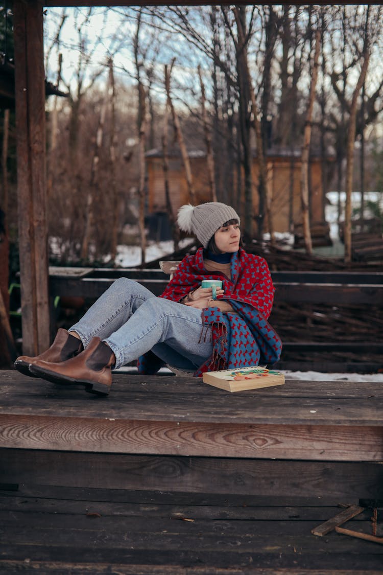 Woman In Winter Clothes Sitting On Wooden Platform 