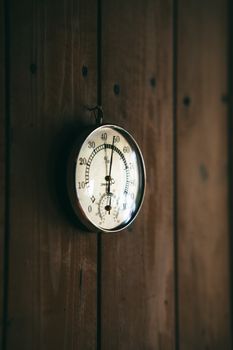 A classic round thermometer mounted on a rustic wooden wall captures a cozy, vintage ambiance.