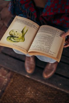 A woman in cozy attire holding an open book with illustrated pages in a relaxed setting.