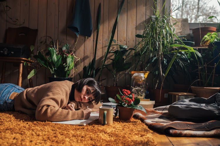 
A Woman In A Sweater Lying Down On A Carpet While Drawing