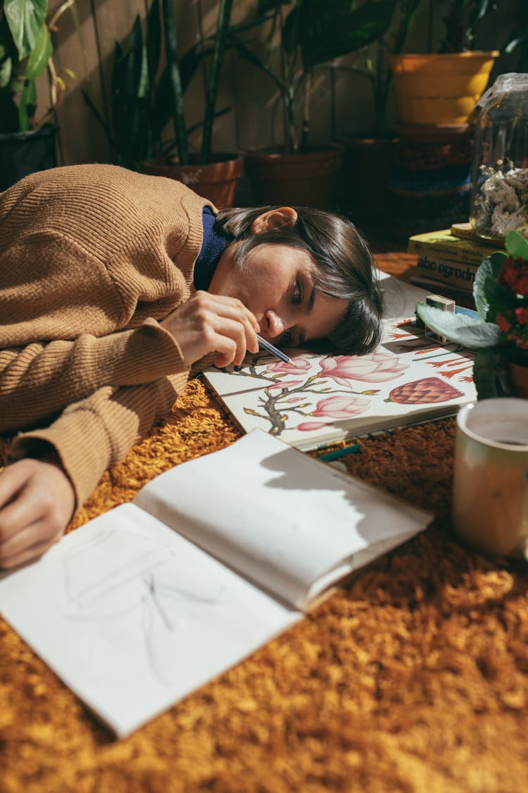 
A Woman In A Sweater Lying Down On A Carpet While Drawing