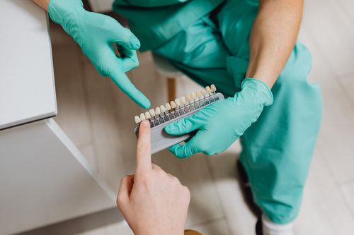 Free A dental professional in gloves holding a teeth shade guide while assisting a patient indoors. Stock Photo