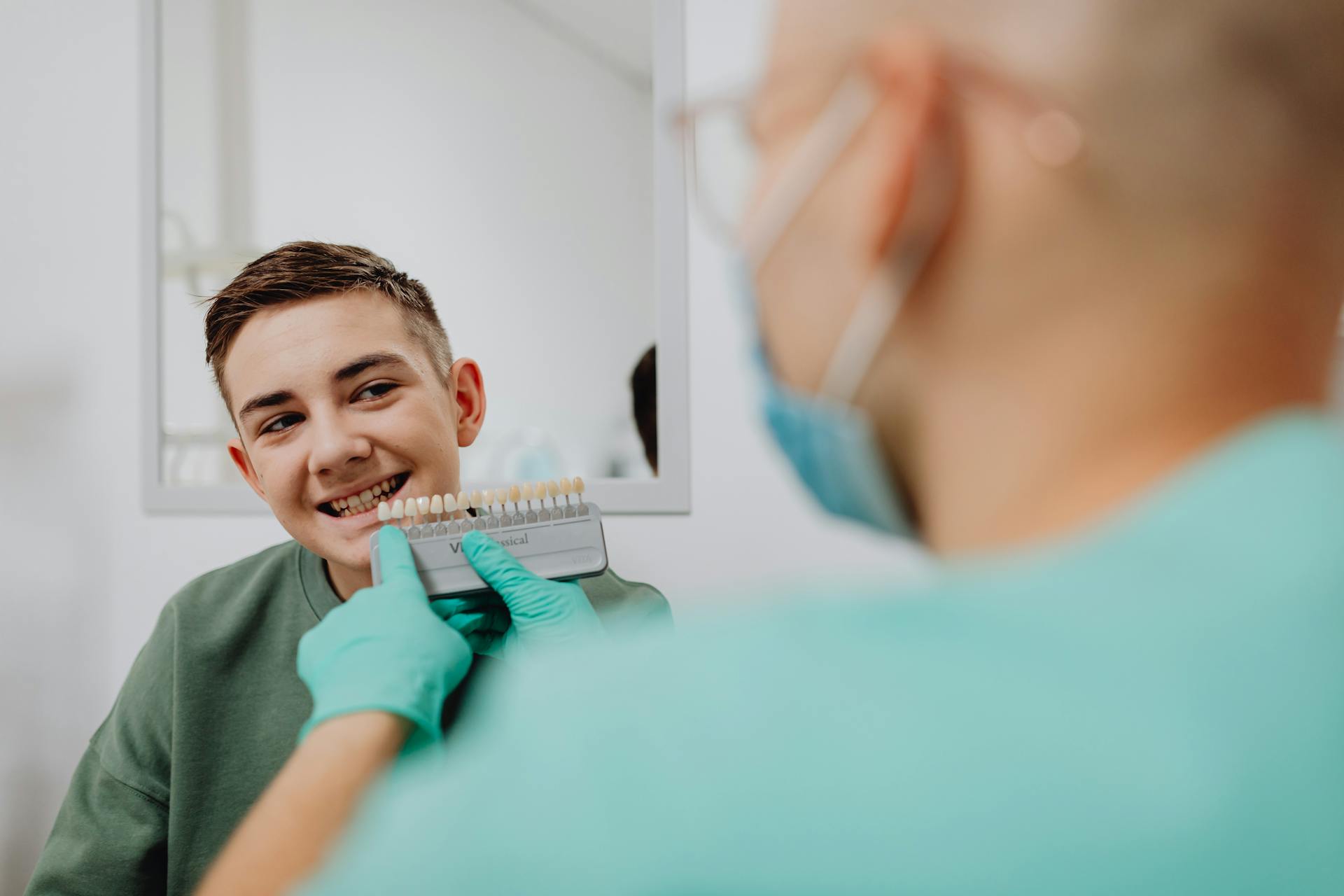 A Boy Smiling while a Person Wearing Latex Gloves is Holding a Dental Shade Guide